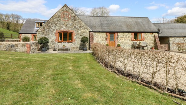 A stone farmhouse with a sloped roof, a wooden bench, and a small garden area. - The Old Dairy (Newport)