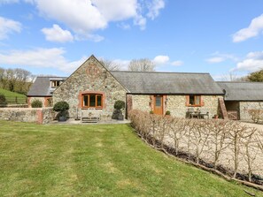 A stone farmhouse with a sloped roof, a wooden bench, and a small garden area. - The Old Dairy (Newport)