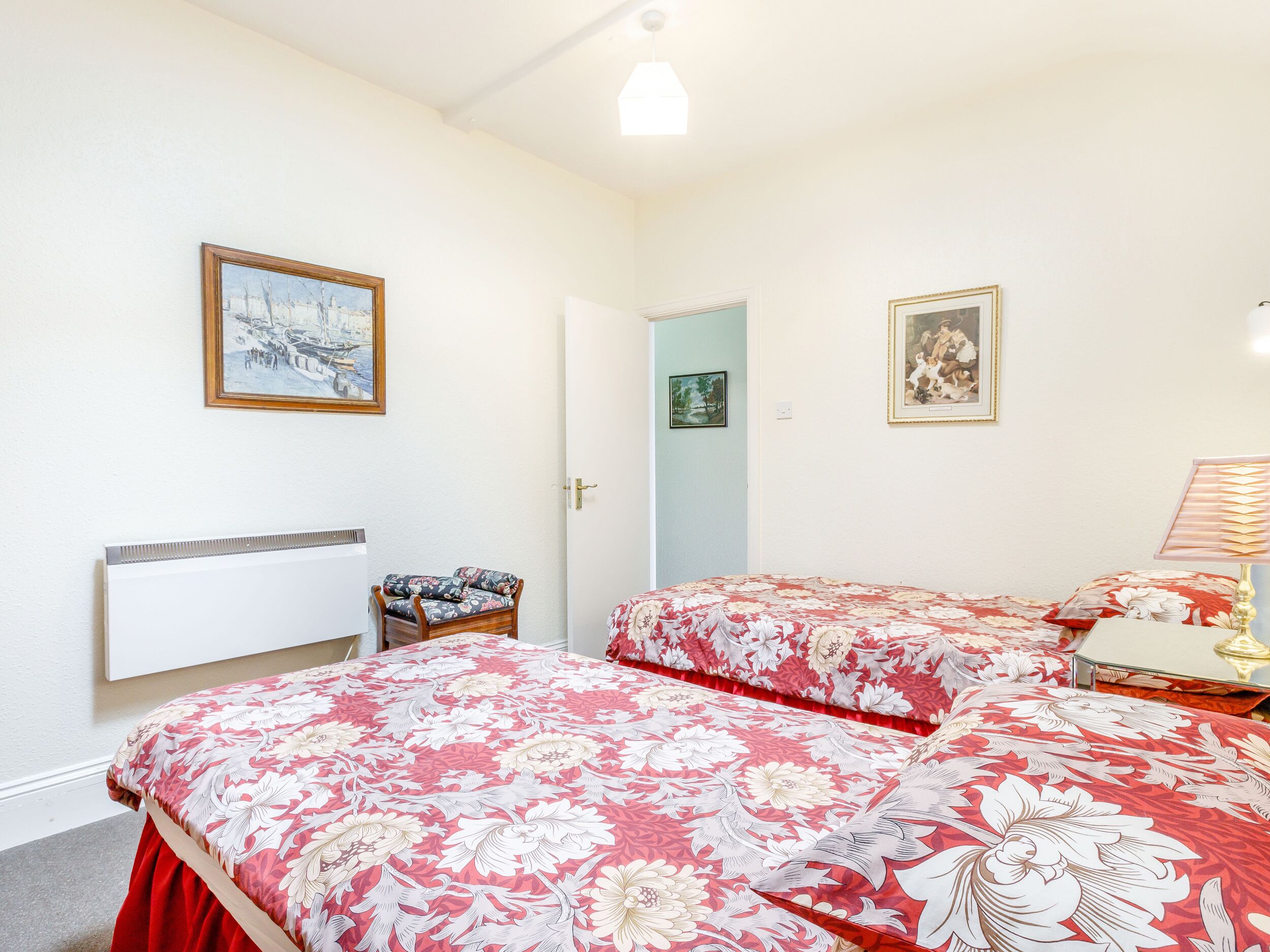 A bedroom with two beds, a chair, and two framed pictures on the wall.