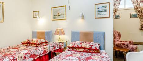 A hotel room with two beds, a desk, a chair, and a window with curtains.