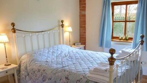 Un llit amb un edredó floral, una taula de nit amb una làmpada i una finestra amb cortines.