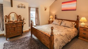 A bedroom with a wooden bed, a dresser, a mirror, and a painting on the wall. - 60 Hyfrydle Road (Caernarfon)
