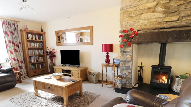 A cozy living room with a stone fireplace, a television, a bookshelf, and a leather sofa. - 60 Hyfrydle Road (Caernarfon)