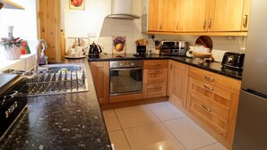 A kitchen with wooden cabinets, a stainless steel refrigerator, a microwave, and a stove. - 60 Hyfrydle Road (Caernarfon)