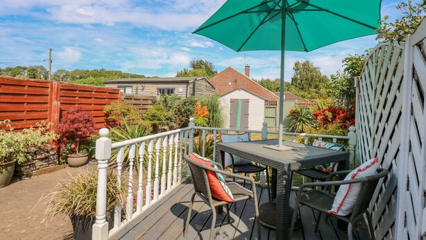 A deck with outdoor furniture, a green umbrella, and a view of a house in the background. - Holly Cottage (Swaffham)
