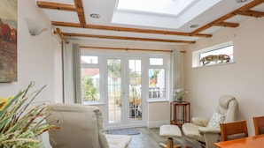 A spacious living room with a high ceiling, wooden beams, a skylight, and a view of the garden through large sliding doors. - Holly Cottage (Swaffham)