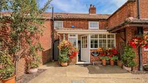 A brick house with a garden, a white door, and a sign reading "Six Dovehouse Row". - Holly Cottage (Swaffham)