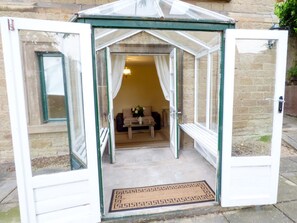 A conservatory with a glass roof, a sofa, a coffee table, and a vase with flowers. - Garden View (Malvern)