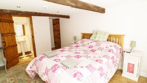 Una camera da letto con un letto a struttura in legno, un comodino con una lampada e una porta che dà su un bagno.