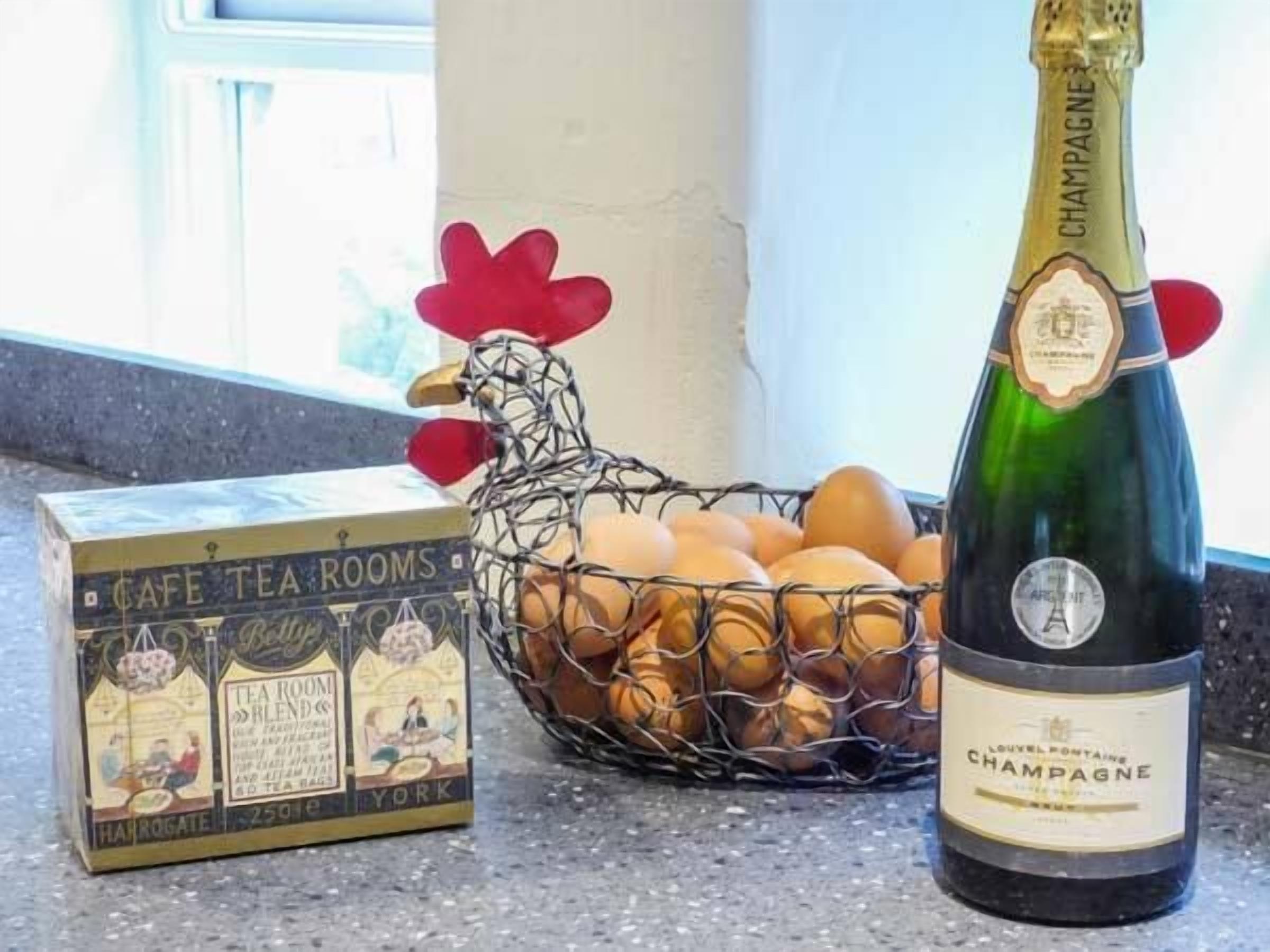 Une bouteille de champagne, une boîte de thé et un panier en fil métallique contenant des œufs, posés sur un plan de travail de cuisine.