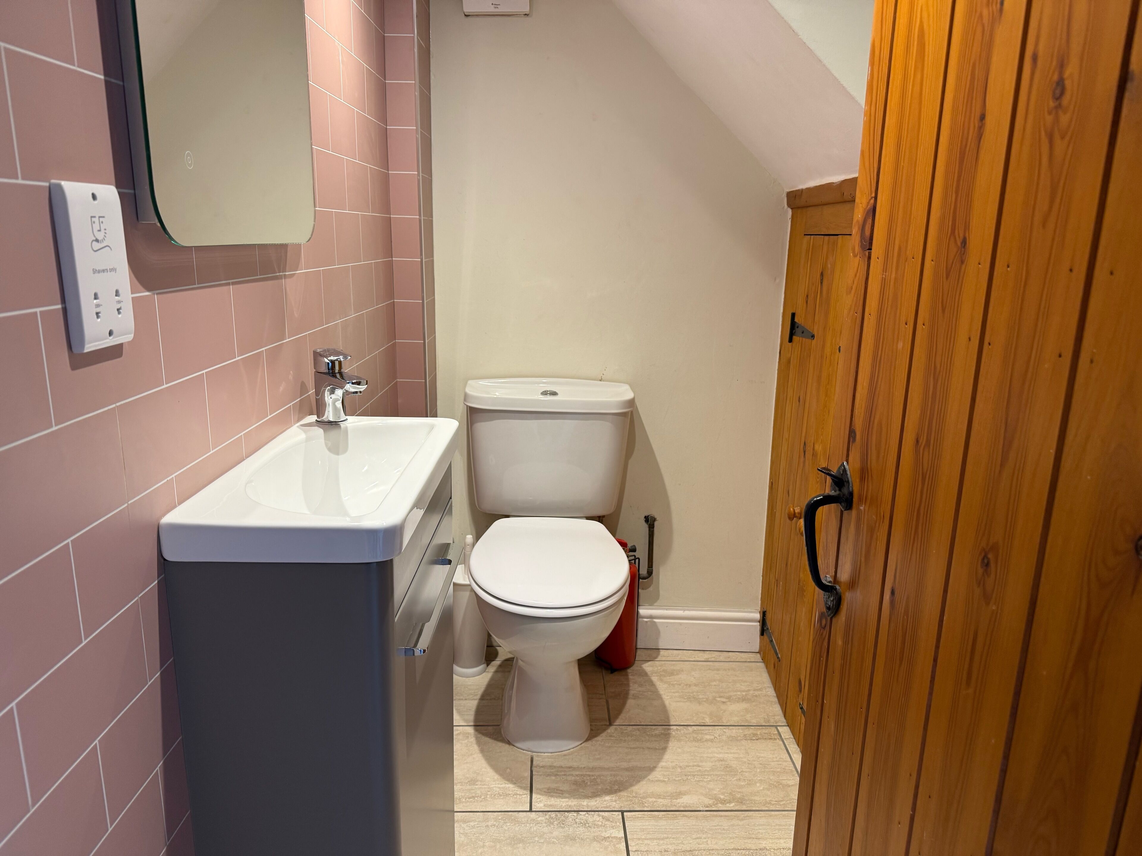 A small bathroom with a white sink, toilet, and wooden cabinet.