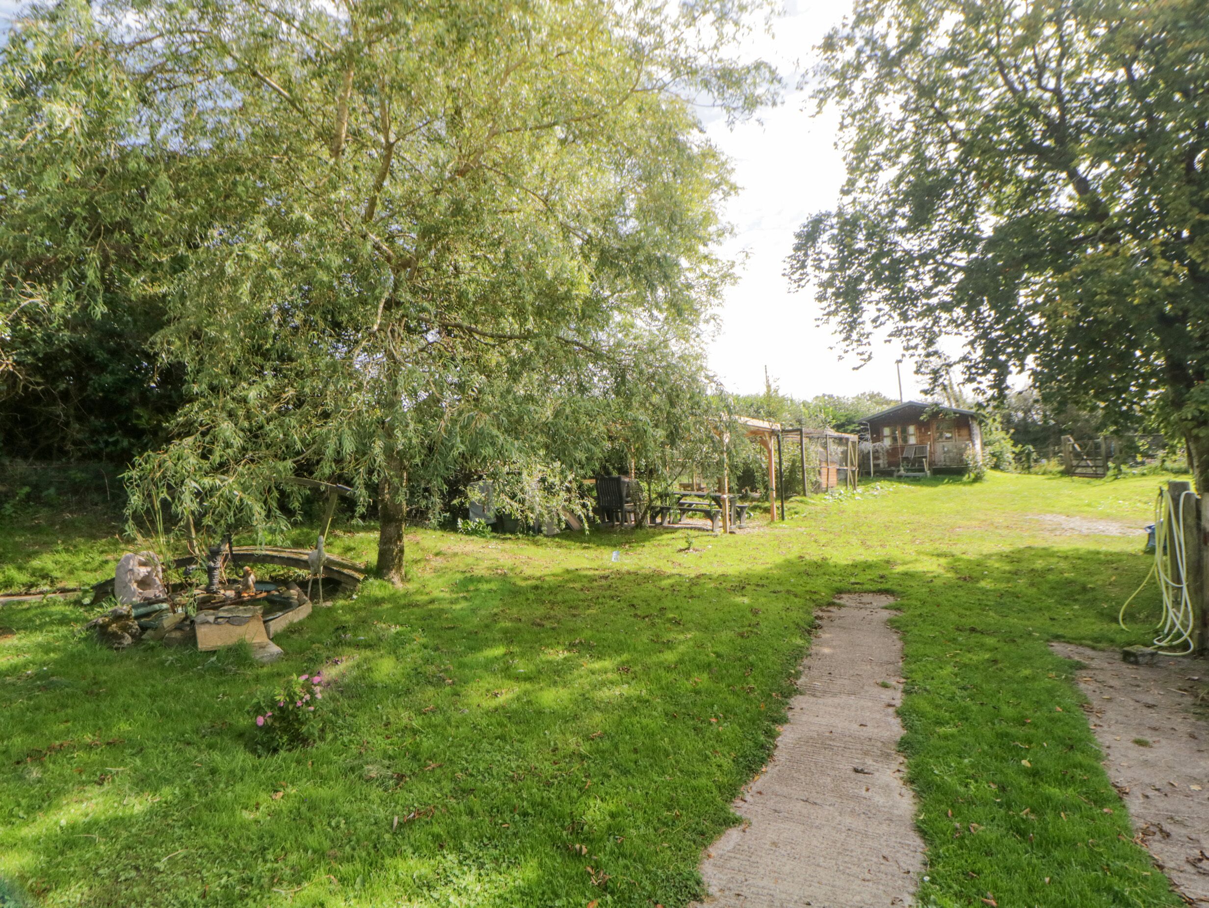 A grassy yard with a wooden swing set, a small pond, and a house in the background.