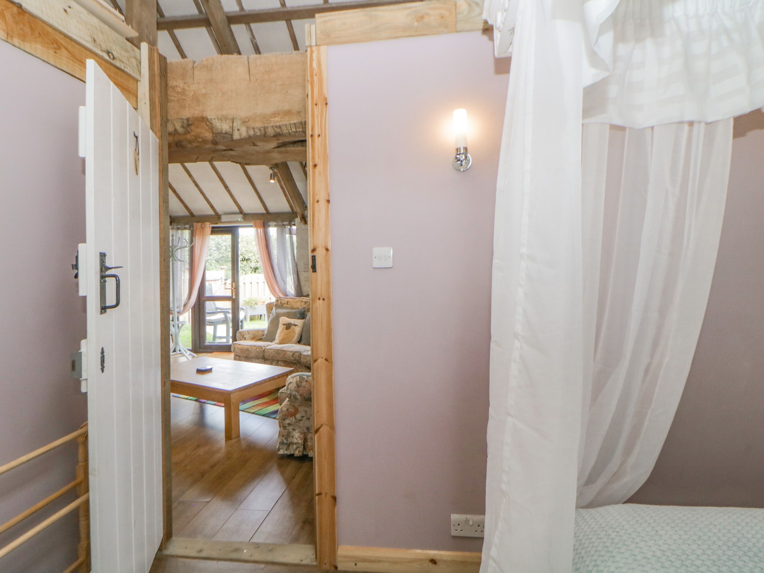 A room with a wooden ceiling, a bed with white curtains, a small table, and a sofa with cushions.