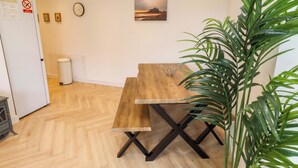 A wooden dining table with a metal centerpiece, a clock on the wall, and a plant in the corner. - Sunrise Cottage (Chathill)