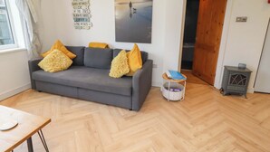 A living room with a grey sofa, wooden flooring, a painting, a small table, and a door. - Sunrise Cottage (Chathill)