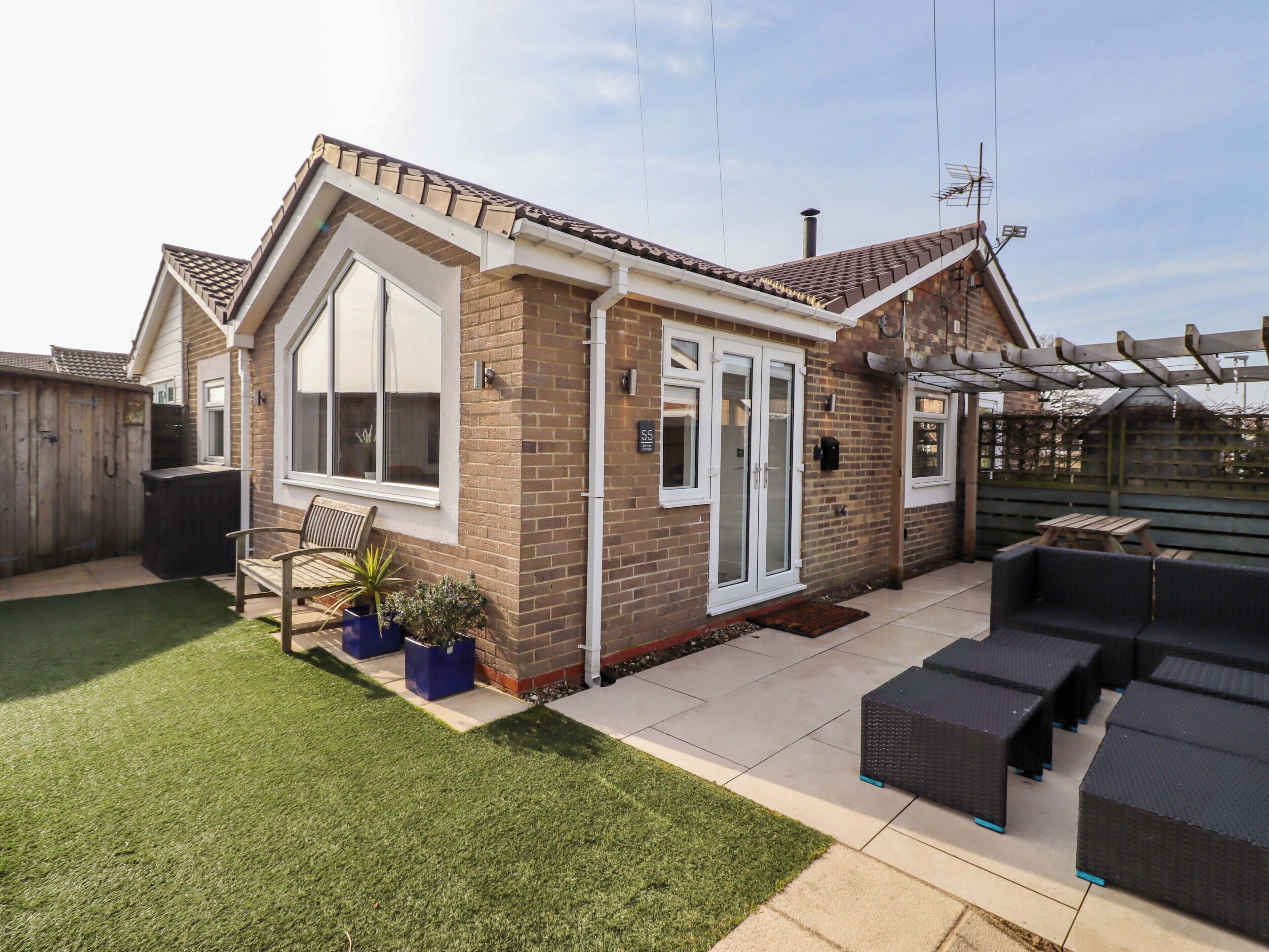 A residential property with a brick exterior, large windows, a patio with outdoor furniture, and a fenced backyard.