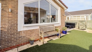 A house with a large window, a wooden bench, and a small lawn. - Sunrise Cottage (Chathill)