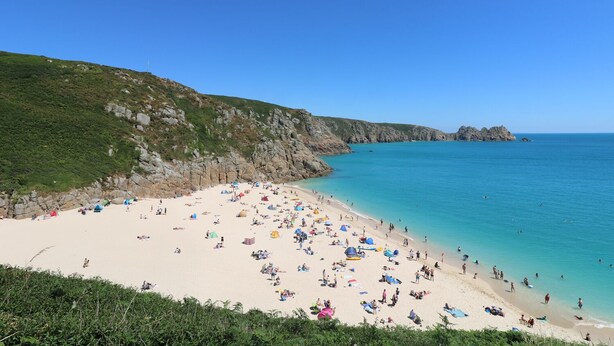 A beach with a rocky cliff, clear blue water, and a sandy shore. - Bell Cottage (Penzance)
