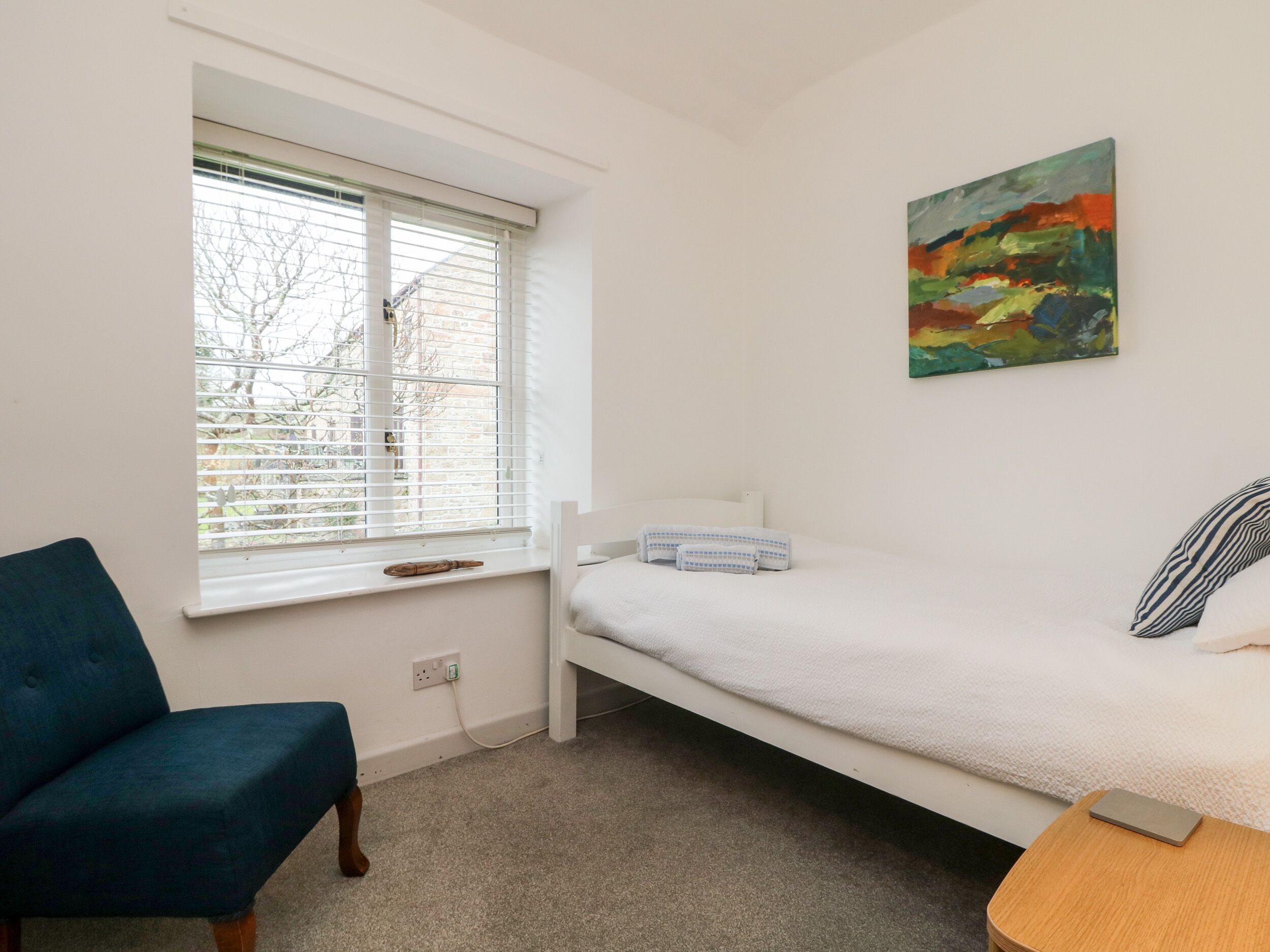 A small, tidy room with a single bed, a chair, a table, and a window with blinds.