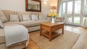 A living room with a beige sofa, a wooden coffee table, and a vase of yellow flowers. - Bell Cottage (Penzance)
