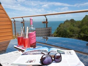 A table with a bottle of rosé, two glasses of red drink, a pair of sunglasses, and an open magazine on a balcony overlooking the sea. - Bayview (Brixham)
