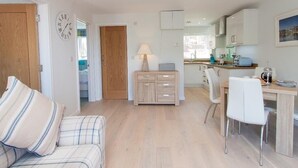 A modern kitchen with white cabinets, a dining table with chairs, and a small seating area with a sofa and a lamp.