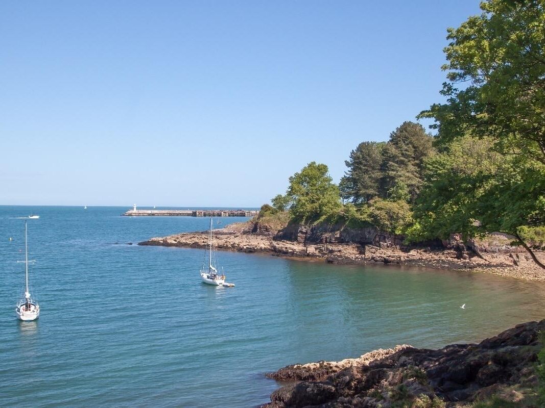 A coastal scene with rocky shores, clear blue water, and a lighthouse in the distance.