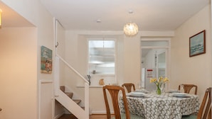 Un coin repas avec une table ronde dressée pour quatre personnes, des chaises en bois, un lustre et un escalier menant à une autre pièce.