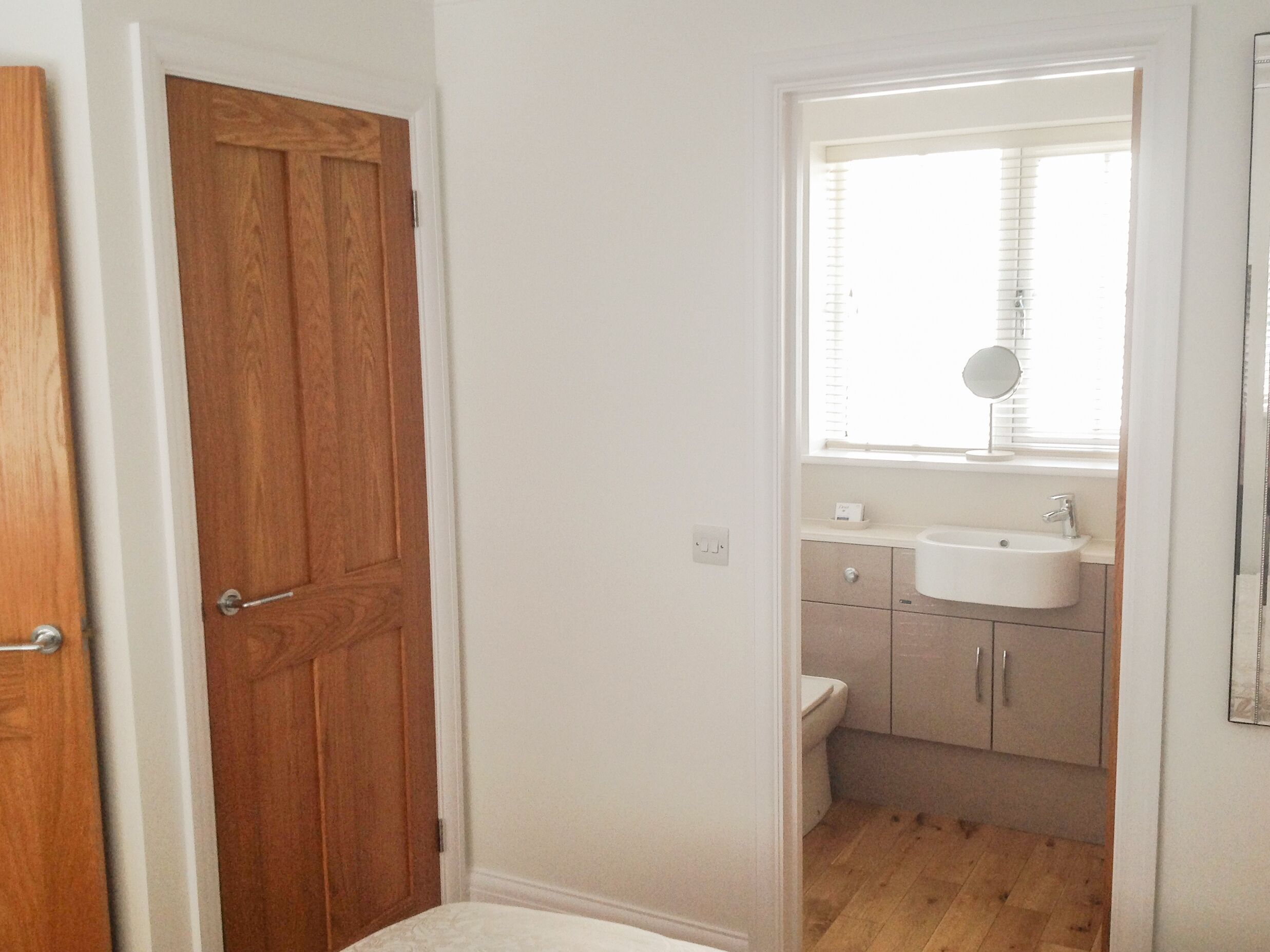 Ein Badezimmer mit Holztür, Waschbecken, Toilette und einem Fenster mit Jalousien.
