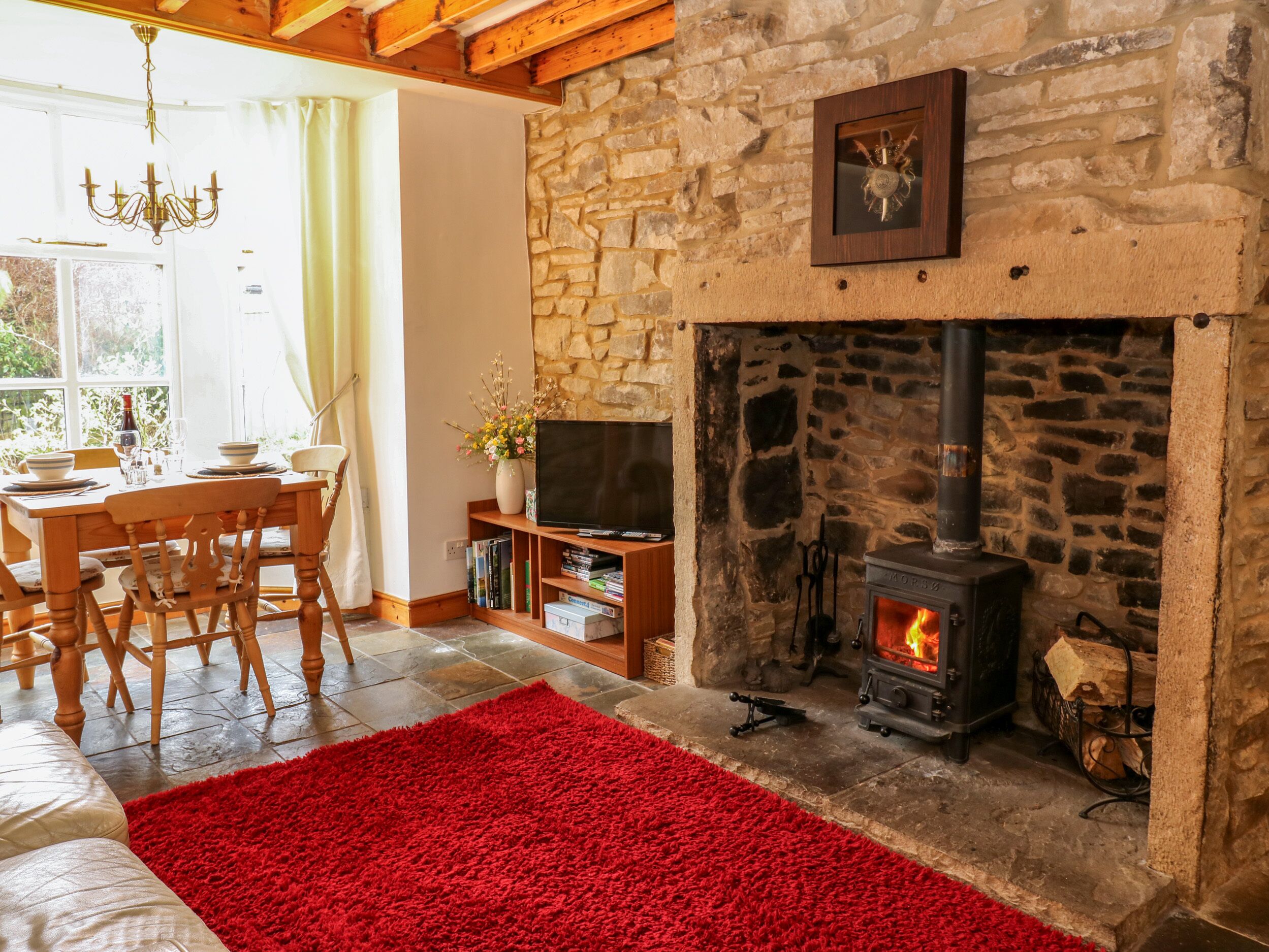 A cozy living room with a stone fireplace, a dining area with a wooden table and chairs, and a television on a wooden stand.