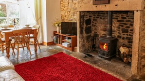 A cozy living room with a stone fireplace, a dining area with a wooden table and chairs, and a television on a wooden stand. - Wayside Cottage (Consett)