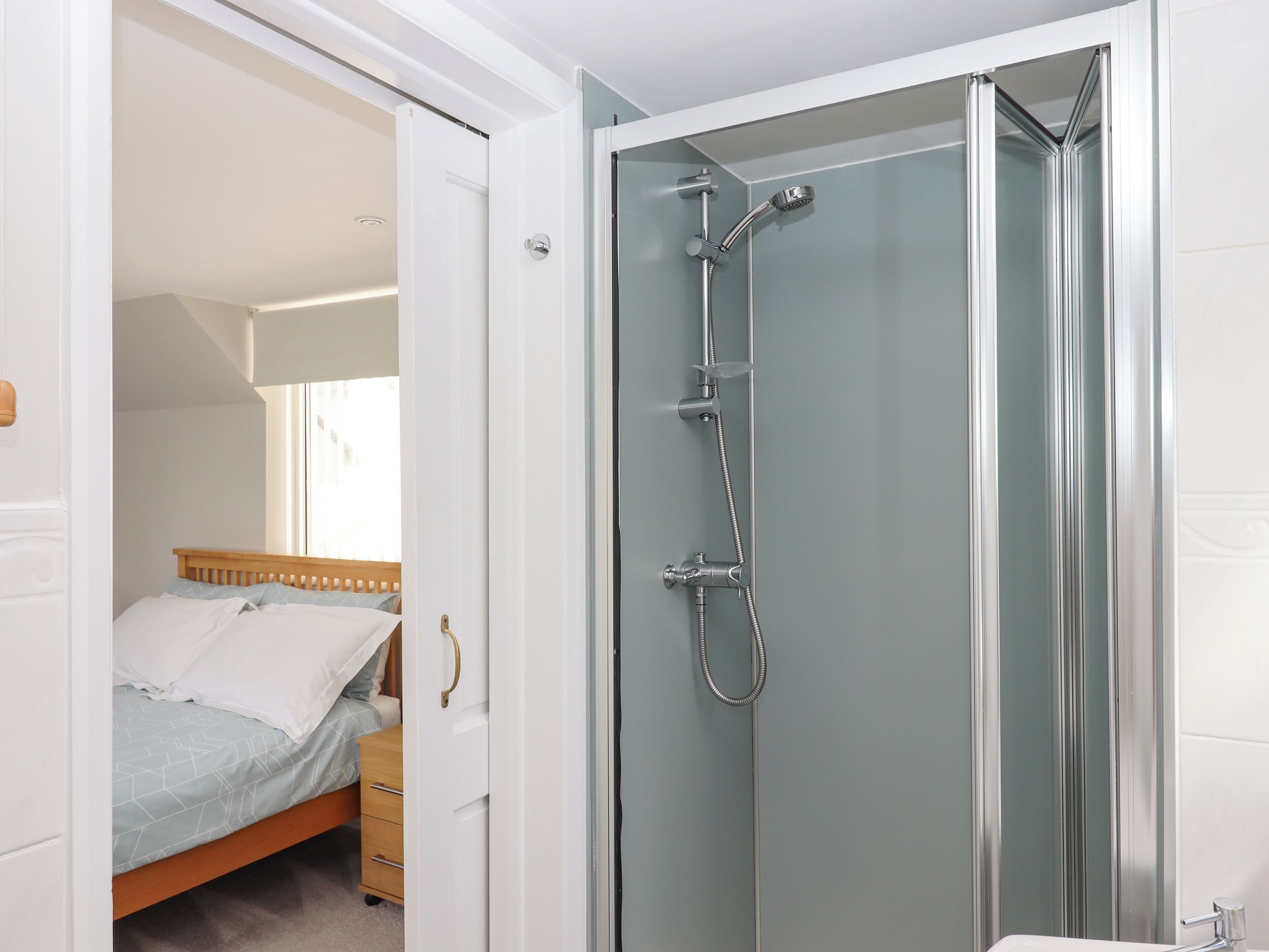 A bedroom with a bed, a wooden dresser, and a glass-enclosed shower area.