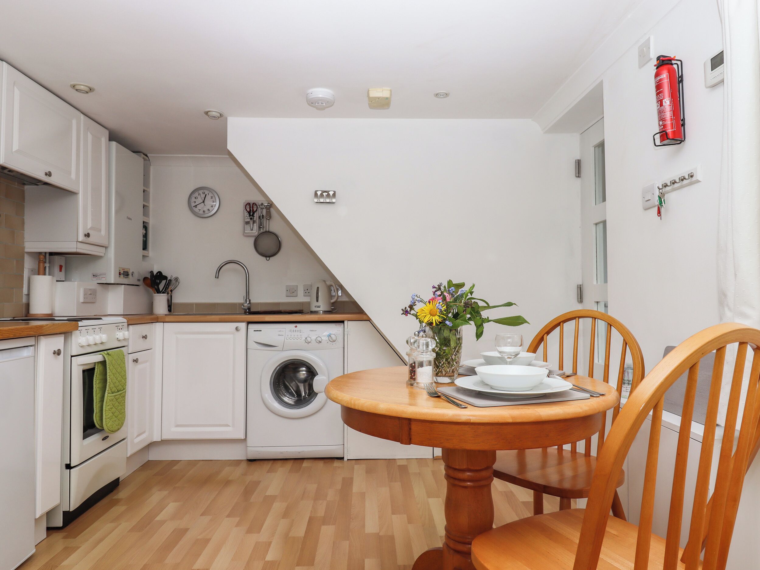 A compact kitchen with a washing machine, a sink, and a dining area with a table and chairs.