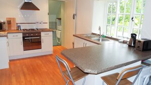A modern kitchen with white cabinets, a granite countertop, a built-in oven, and a window with a view of greenery. - The Granary (Ross-on-Wye)