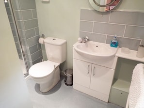 A bathroom with a toilet, sink, and a small trash bin. - The Granary (Ross-on-Wye)