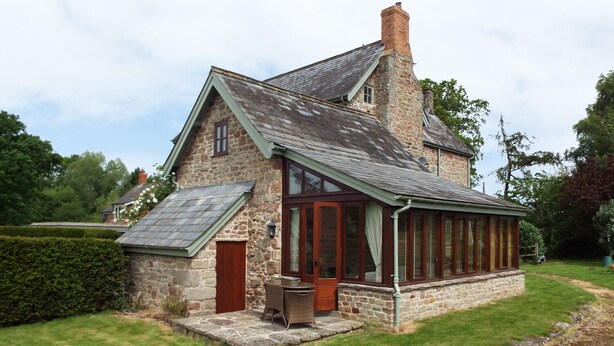 A stone house with a sloped roof, a wooden door, and a covered porch with windows. - The Granary (Ross-on-Wye)