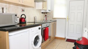 A compact kitchen with a washing machine, a microwave, a kettle, and a sink.