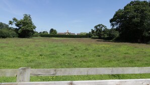 A grassy field with a wooden fence in the foreground and a building in the background.