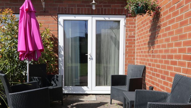 A patio with wicker furniture and a pink umbrella, a sliding glass door, and a brick wall.
