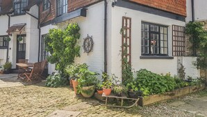 A traditional white building with a red-tiled roof, a wooden door, and a small garden area with potted plants and a wooden bench. - The Coach House (Newport)