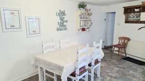A dining area with a table and chairs, a wall-mounted shelf with dishes, and framed artwork. - The Coach House (Newport)