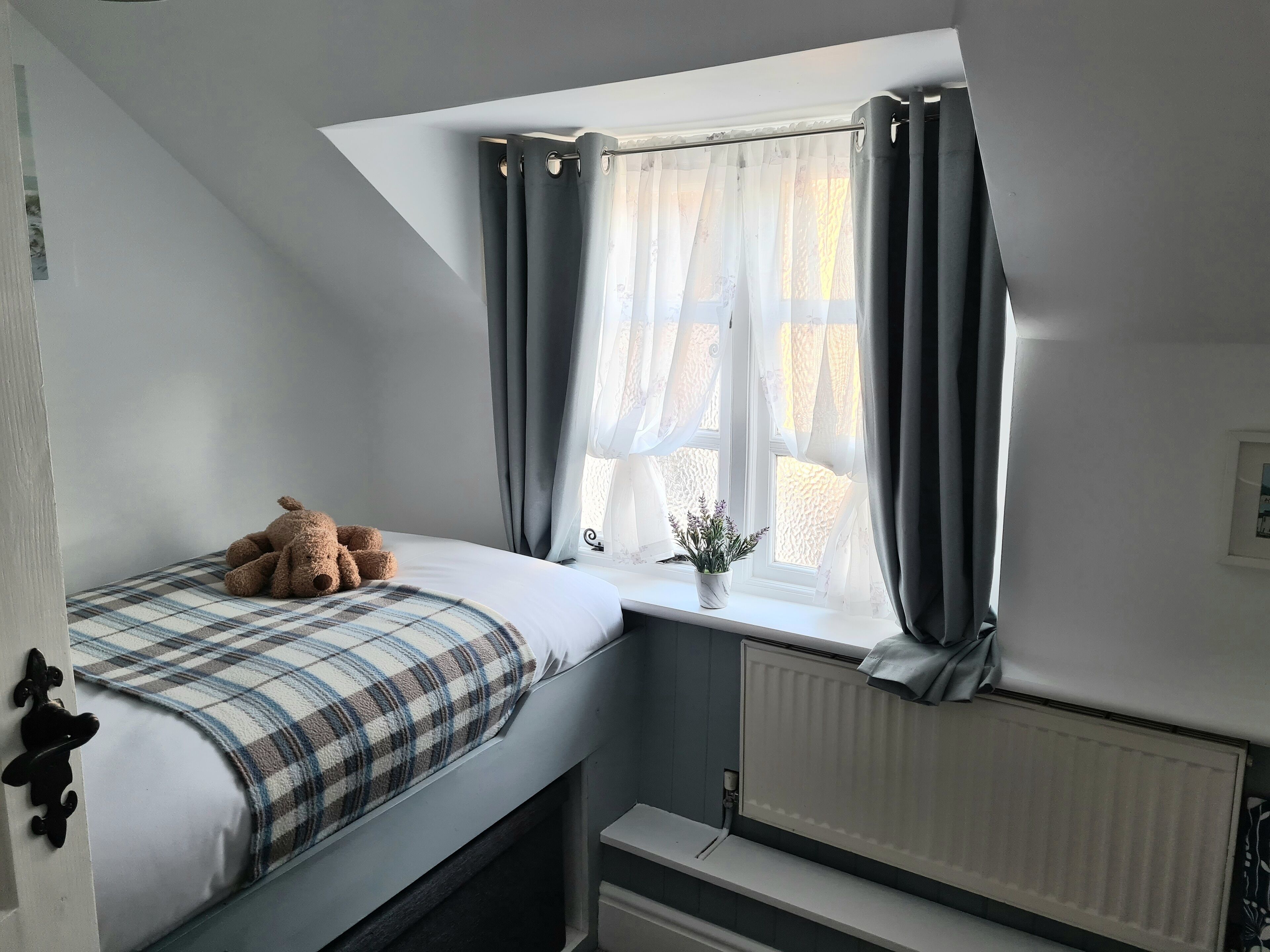 A bedroom with a bed, a window with curtains, a radiator, and a small plant on the windowsill.