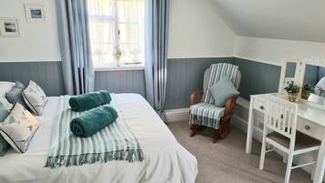 Ein Schlafzimmer mit Bett, Stuhl, Schreibtisch und einem fenster mit Vorhängen.