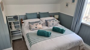 A neatly made bed with striped bedding, two pillows with bird patterns, a teal throw blanket, and a bedside lamp. - The Coach House (Newport)