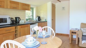A modern kitchen with wooden cabinets, a microwave, and a coffee maker. There is a dining table with chairs and a small sofa in the living area. - Lakeside Lodge (Norwich)