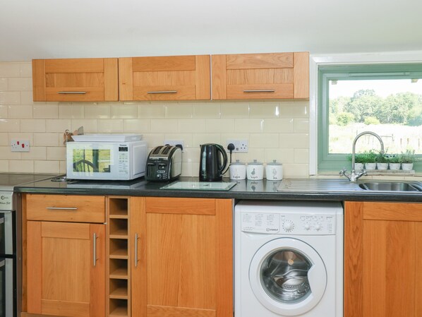 A compact kitchen with wooden cabinets, a microwave, toaster, kettle, and a washing machine. - Lakeside Lodge (Norwich)
