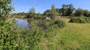 A serene lakeside setting with a small wooden structure, surrounded by lush greenery and trees. - Lakeside Lodge (Norwich)