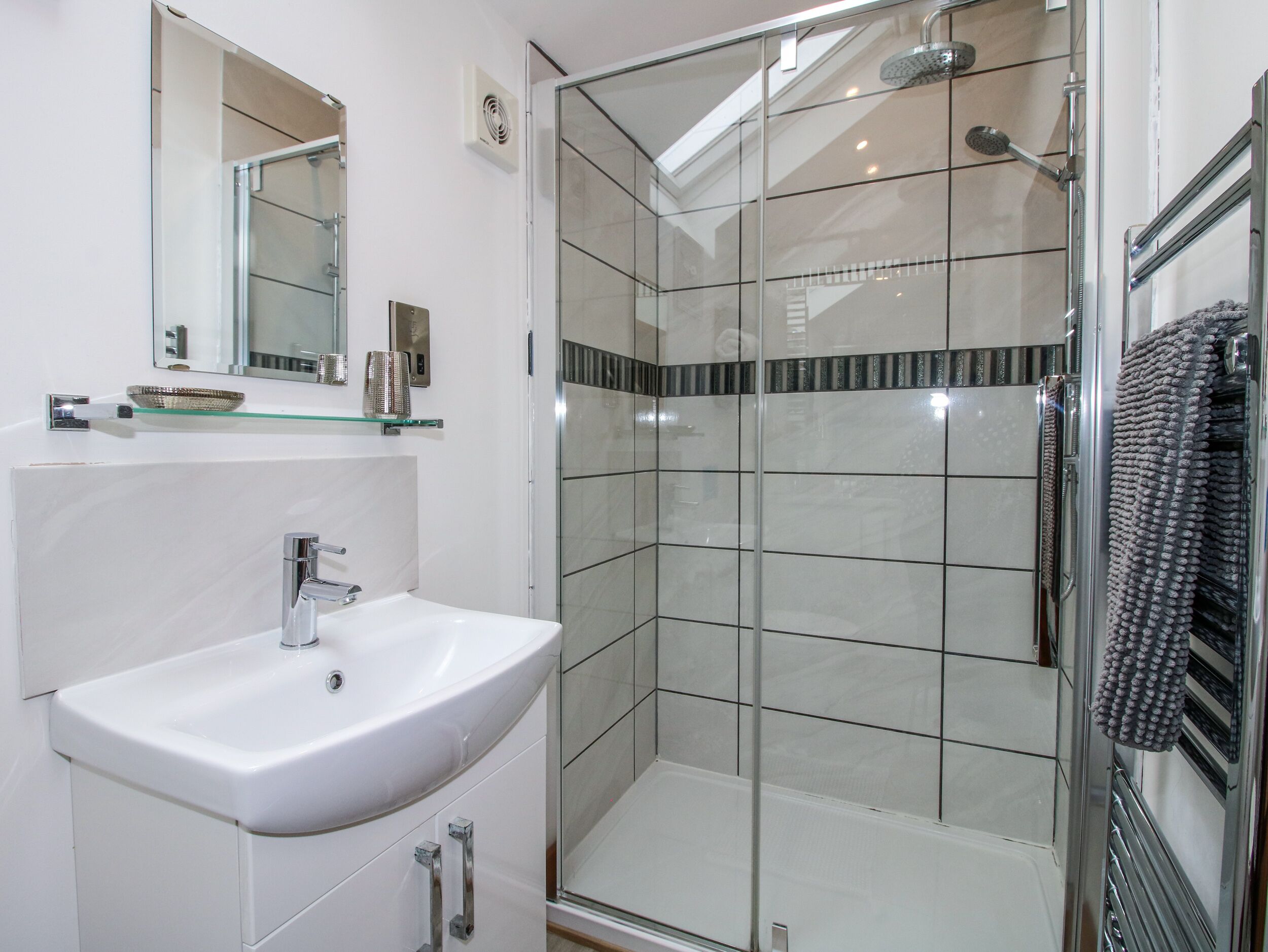 A modern bathroom with a glass shower enclosure, a white sink, and a mirror above it.