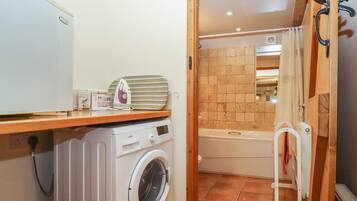 A compact laundry room with a washing machine, an ironing board, and a bathtub.