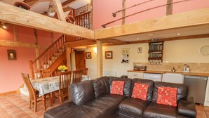 A spacious living area with a leather sofa, wooden dining table, and a staircase leading to an upper level. - The Old Stables (Ross-on-Wye)